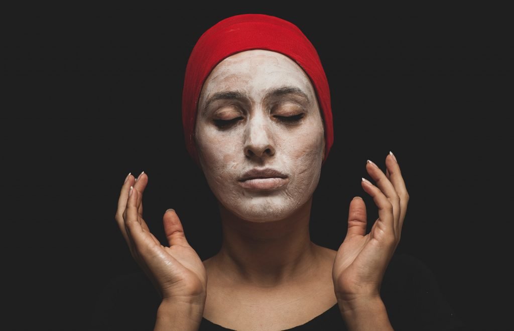 female presenting person wearing a red hijab. Her face is covered in a skincare product.